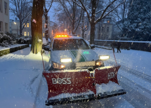 Einsatzfahrzeug mit Schneeschieber räumt abends bei Schneefall die Straße.