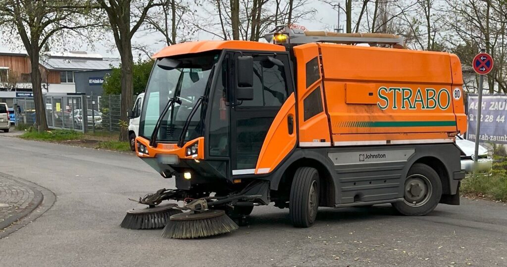 Große orange Kehrmaschine von vorne bei der Straßenreinigung, Schmutz entfernen im Einsatz.
