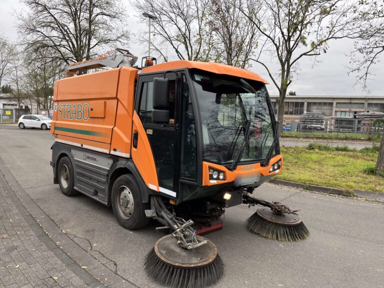 Orange Kehrmaschine von vorne auf der Straße bei der Straßenreinigung.