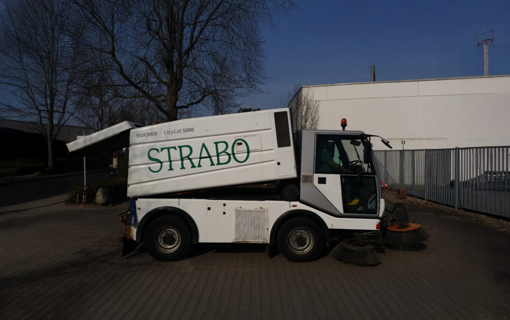 Weiße Kehrmaschine mit Logo im Einsatz für die Straßenreinigung.